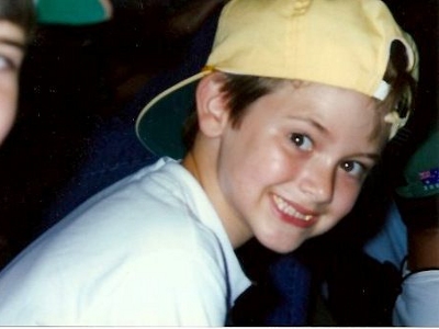 Craig as a child smiling with a yellow baseball hat on backwards (Credit: Janet Denison)