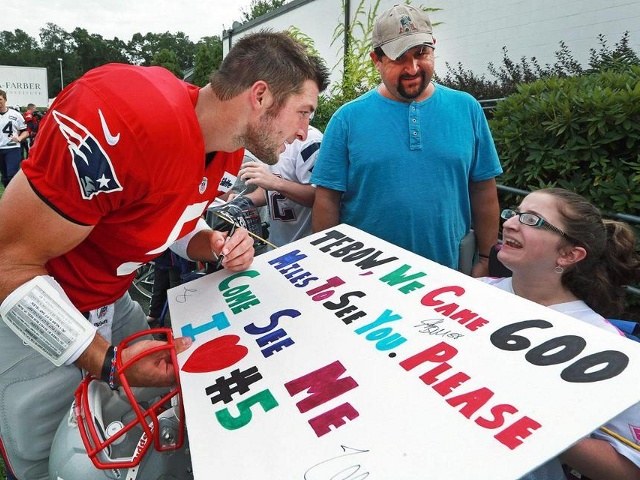After asking her name, Tim Tebow autographs the poster of wheelchair-bound Madelin Beardsley of Virginia Beach, as her father Scott looks on, August 5, 2013 (Credit: Boston Globe/Jim Davis)