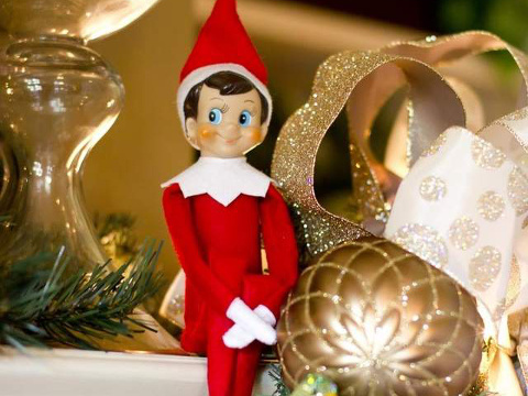 The Elf on the Shelf sitting on a mantle surrounded by Christmas decorations (Credit: CCA&B, LLC)