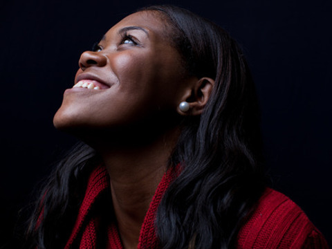 A young woman wearing a red sweater for Christmas looking up to God and smiling (Credit: Pearl via Lightstock)
