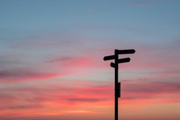 A shadowed wooden directional against a sunset sky of pink and purple hues