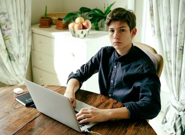An adolescent boy in front of a computer, looking up with a blank stare.