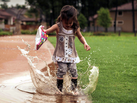 A little girl, who prayed for rain, jumps and splashes in puddles outside her home while it rains, May 14, 2015 (Credit: Chris Partheniou via Flickr)