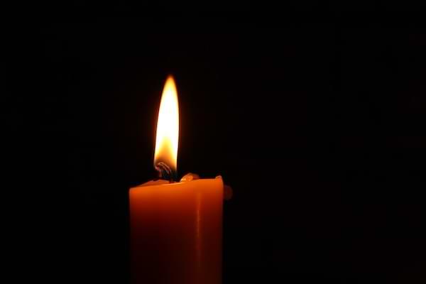 A burning red candlestick candle in front of a black backdrop