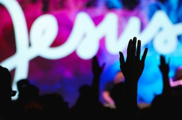 Contemporary worship service with shadowed hands lifted in the air praising Jesus.