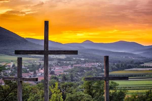 Three crosses at sunrise with mountains and fields in the background