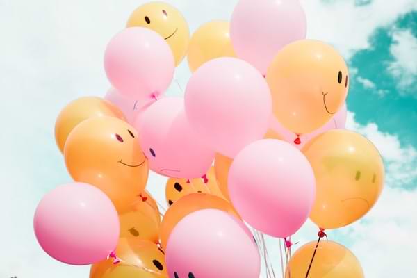 A bunch of pink and yellow balloons with smiling and frowning faces on them floating in the air.