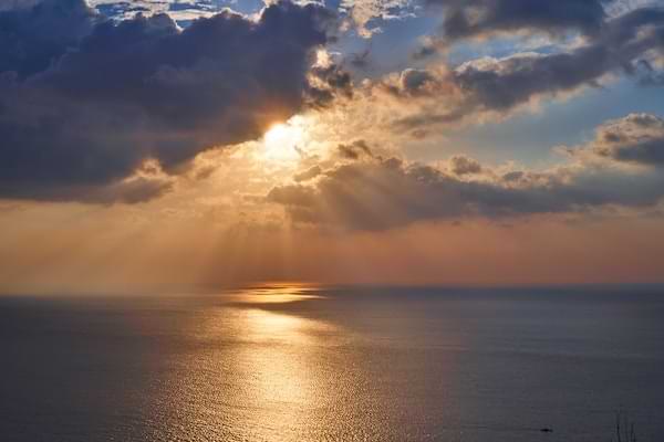 Golden rays from the sun peeking out from clouds and reflecting off of a calm ocean