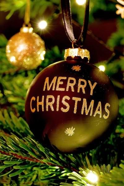 A red glass round ornament that says Merry Christmas, hanging on a Christmas tree