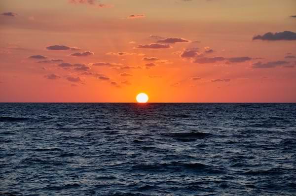 A sun setting over the ocean, displaying a brilliant orange and red skyline