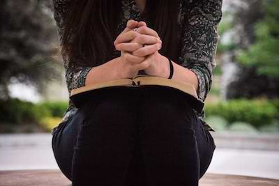 A women sitting on a bench, with an open Bible in her lap and her hands clasped together in prayer, as if praying, Dear, Lord: I'm ready to listen