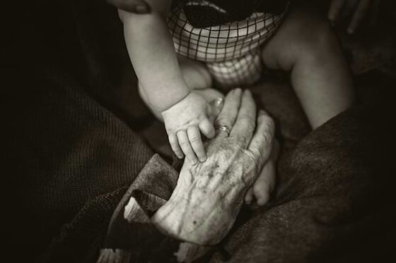 Black and white image of a young baby's hand on top of an old woman's outreached hand