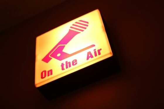 A gold-lit sign with a red microphone and the words "On the Air" indicating a broadcast is in play
