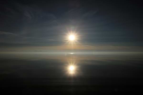 The rising sun casting light against a dark sky and ocean