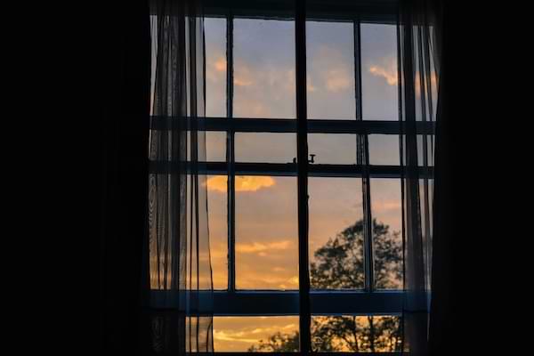 A sheer-curtained window, revealing a golden-hued dusk sky