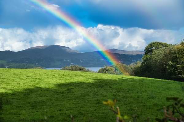 A Rainbow arching over a green field with mountains in the background.