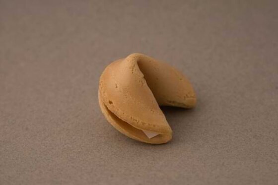An unopened fortune cookie sitting on a neutral colored surface.