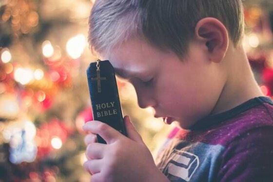 A young boy praying with his forehead pressed against the Holy Bible