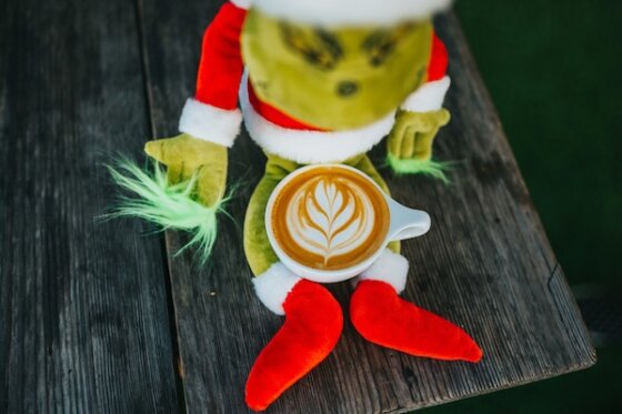 A stuffed grinch in a Santa suit with a pumpkin spice latte in his lap