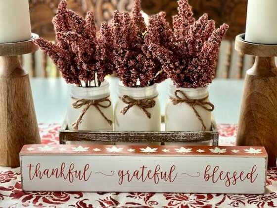 Three small jars filled with dried rust-colored fronds adorn a wooden plaque that says, "thankful grateful blessed."