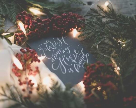 Surrounded by red Christmas berries and evergreen, a small black chalkboard ornament says "In Christ Alone my Hope is Found" written on it.