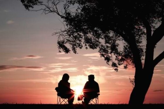 A man and woman sitting under a tree watching the sunrise