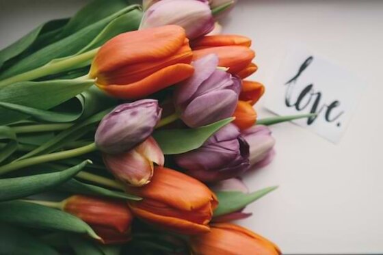A bundle of orange and purple tulips laying horizontally on a table next to the word "love"