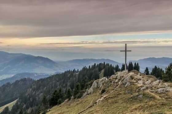 A rocky hill with a wooden cross atop and a mountainous skyline at dusk