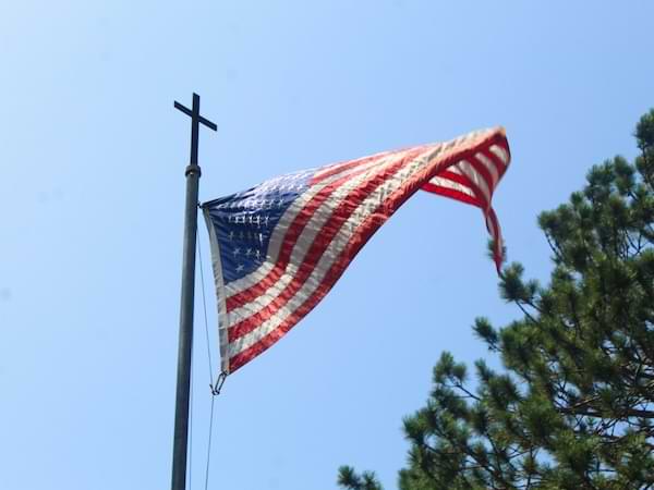 A US flag flying under a cross atop the flag pole