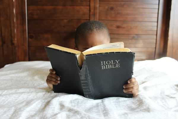 A young African-american boy in bed, reading a tattered Holy Bible