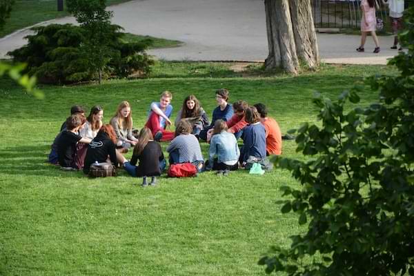 Group of young adults sitting in a circle on a patch of grass in a park.