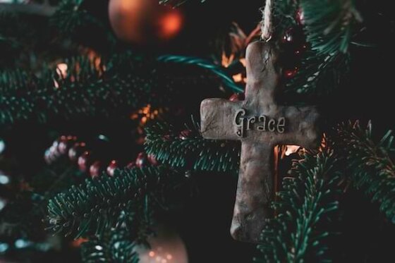 A close up view of a Christmas tree branch with a cross ornament that has the word grace in the center