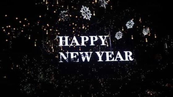 The words, "Happy New Year" in white on a black backdrop patterned with light snowflakes, lights and tinsel