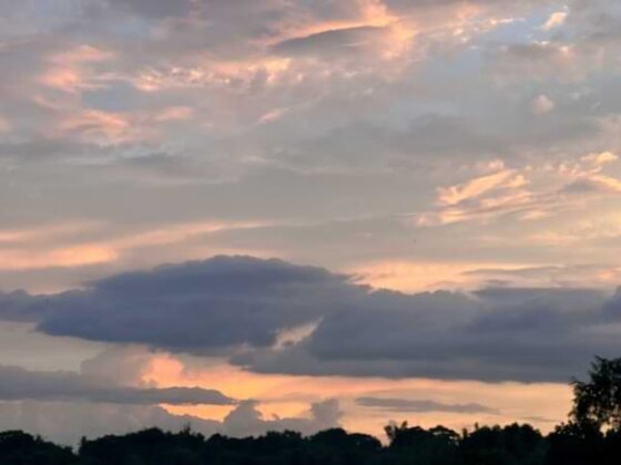 A cloud-covered horizon with bursts of pale orange and pink filtering through as the sun rises